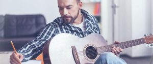 Man writing music on acoustic guitar